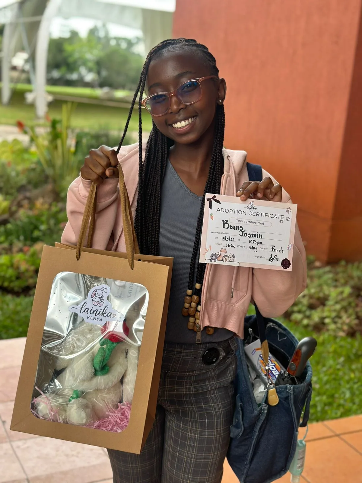 A young woman smiling and holding up an adoption certificate for her plushie named Beans