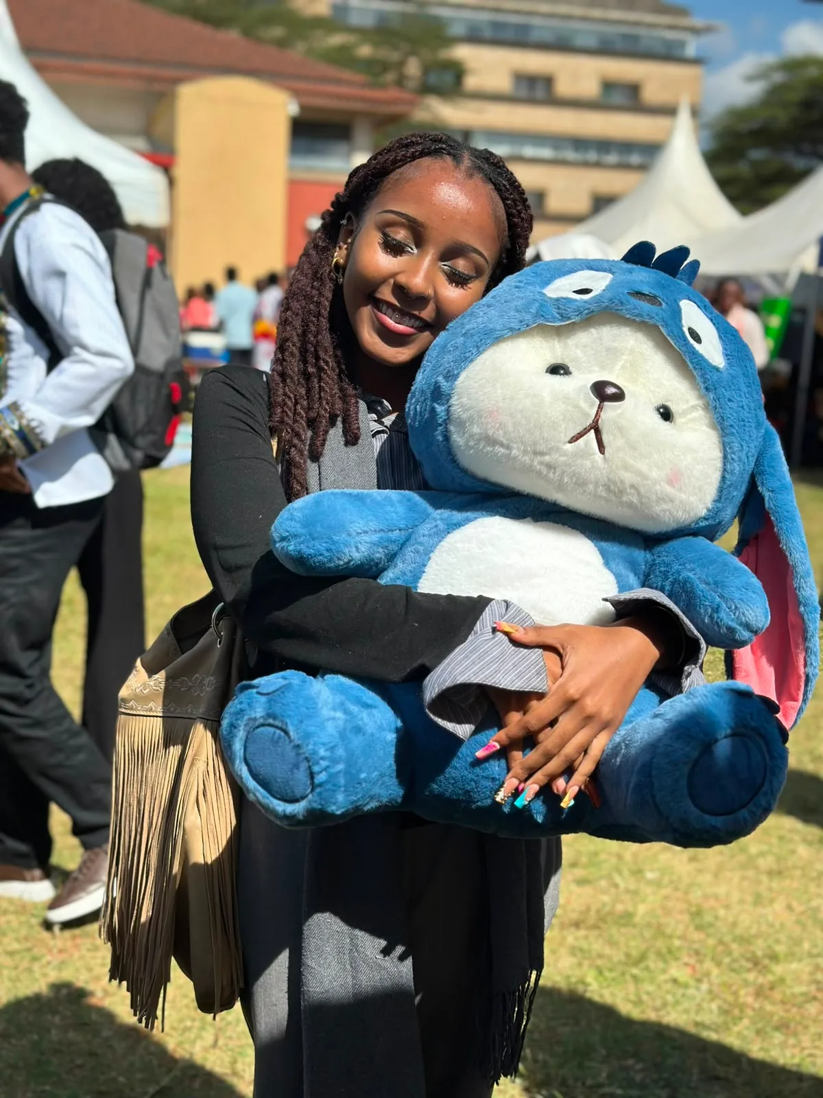 A woman smiling while cradling a giant blue and white plushie at an outdoor event