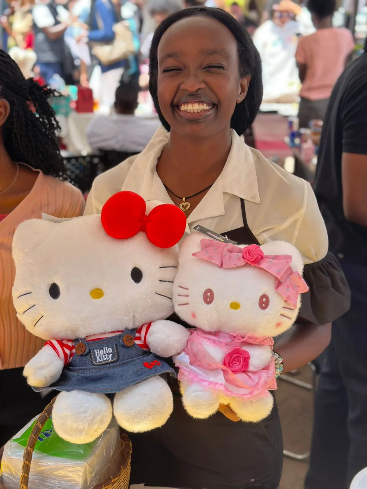 A woman laughing while holding two Hello Kitty plushies