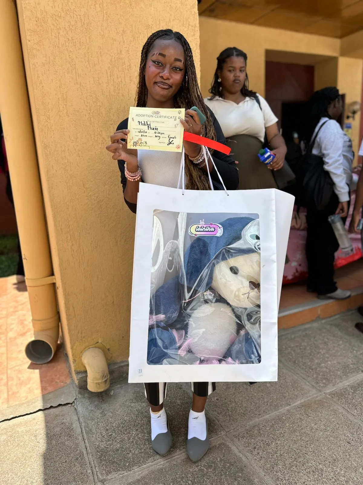 A woman smiling and holding an adoption certificate for her plushie named Nikki