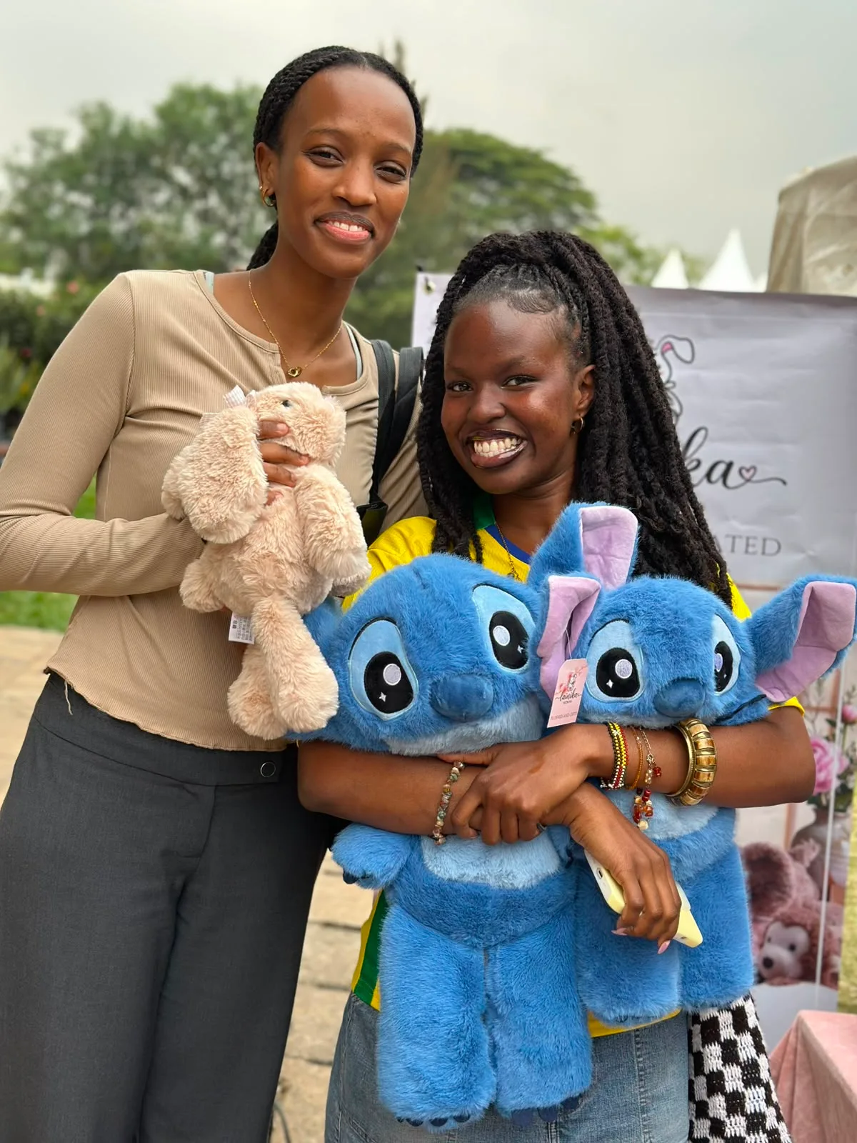Two women smiling at the Lainika pop-up stall, holding a bunny plushie and two Stitch plushies