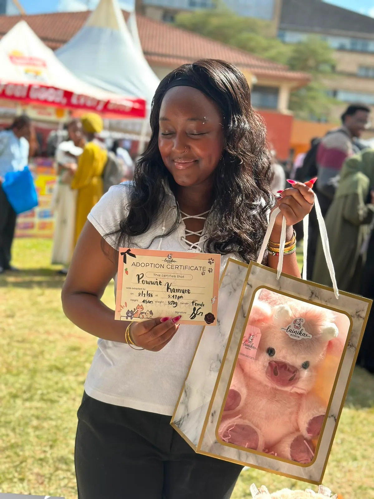 A woman smiling and holding an adoption certificate for her pink plushie named Powwie