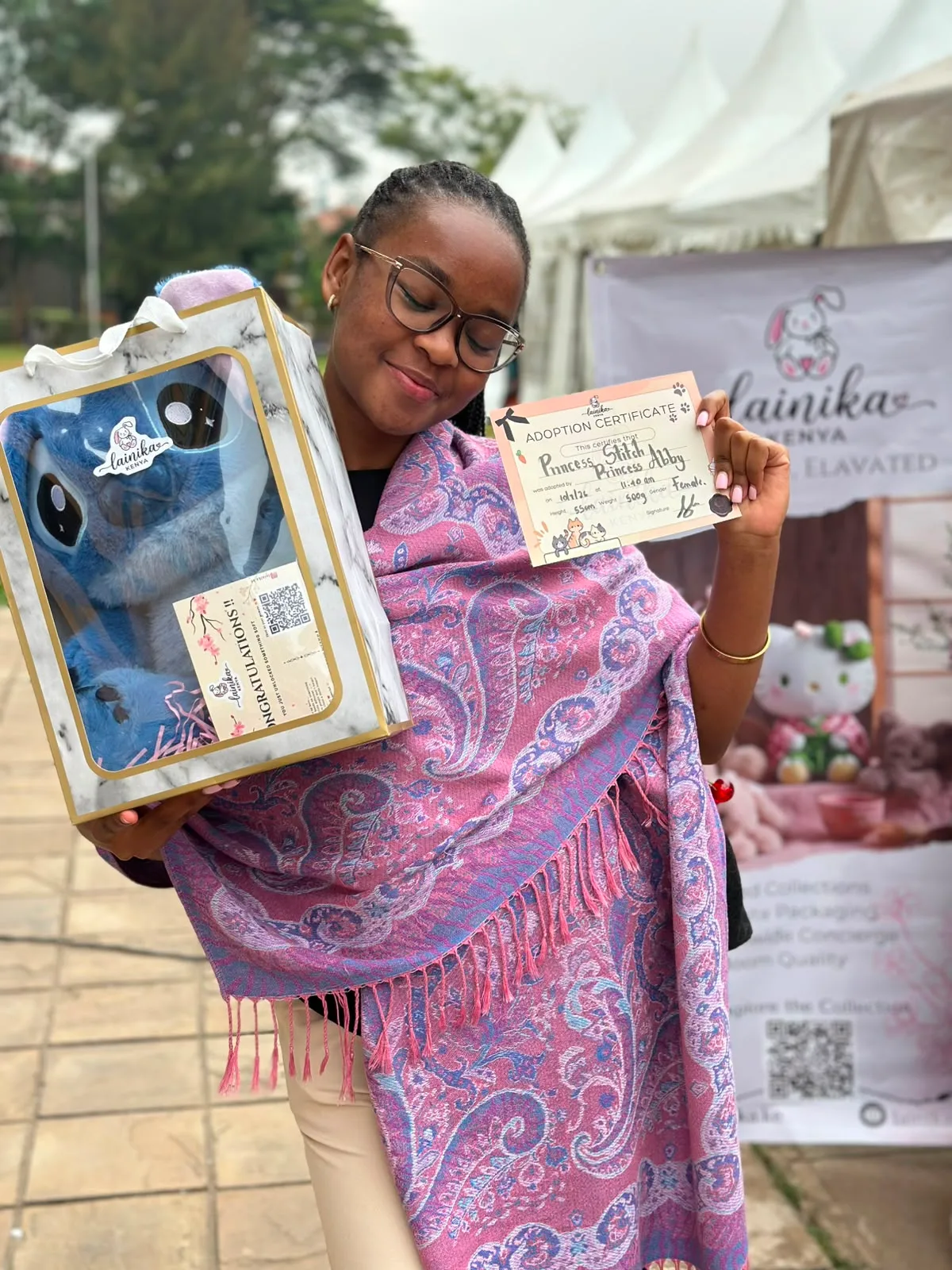 A woman at the Lainika stall smiling while holding an adoption certificate for an XL Stitch plushie